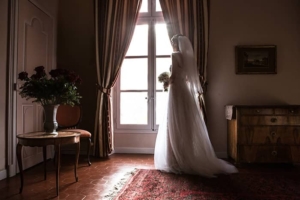 La mariée tenant son bouquet devant la fenêtre.
